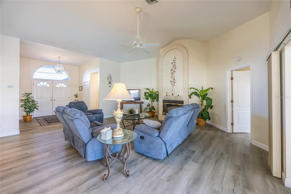 A living room features blue reclining furniture, a fireplace, and light wood-look flooring — 3316 SE 19TH PLACE, CAPE CORAL, FL