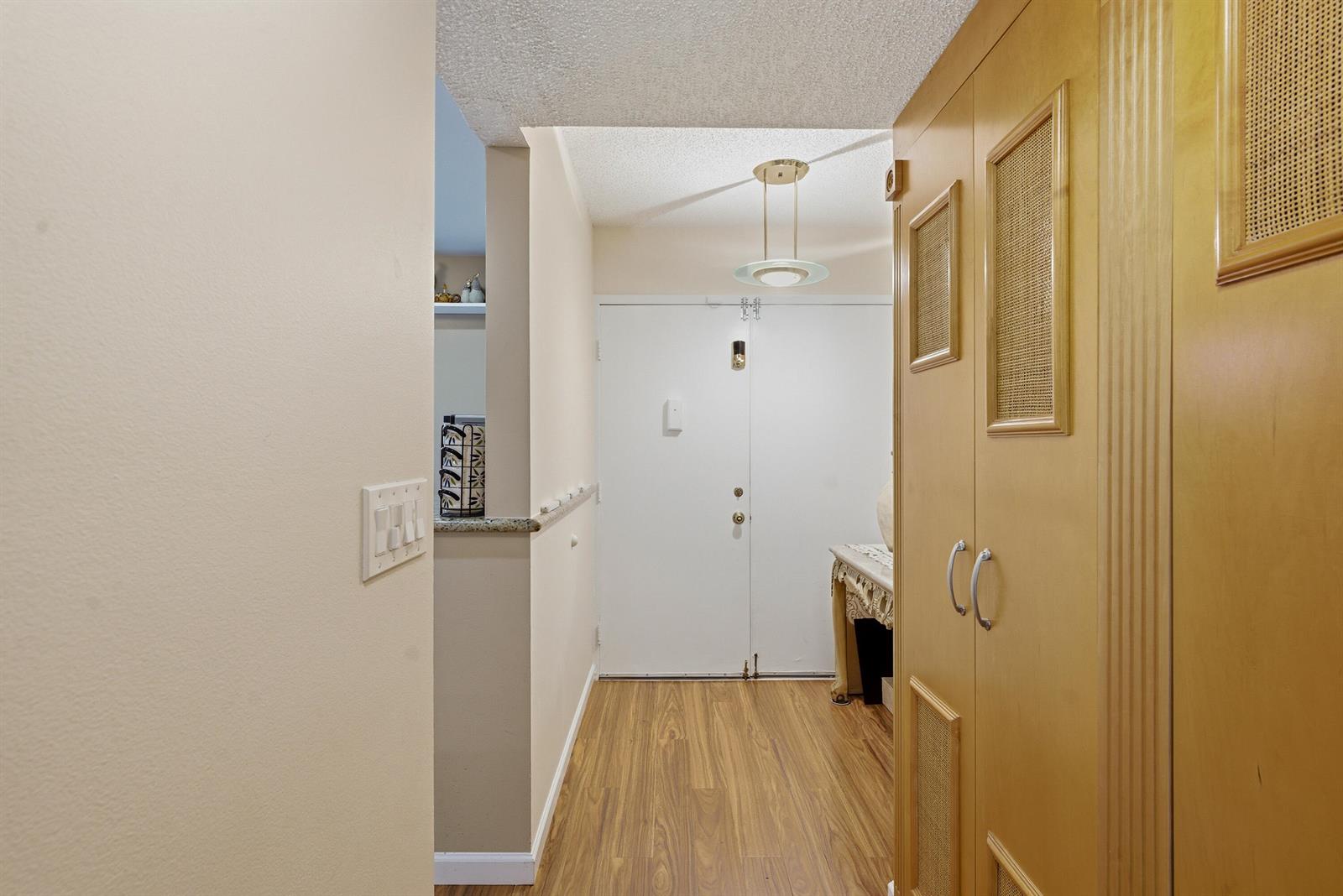 An entryway features wood-look flooring, a light-colored wall, and a large wooden storage cabinet — 3286 Arcara Way # 306, Lake Worth FL 33467, LAKE WORTH, FL