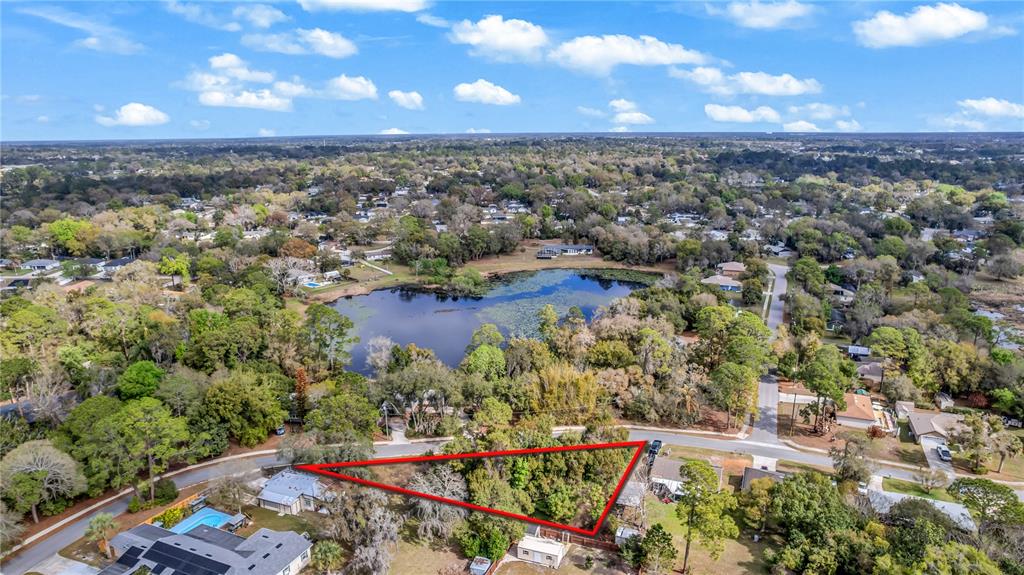 An aerial view shows a triangular vacant lot bordered by roads and trees near a lake — 205 PLUMOSA ROAD, DEBARY, FL