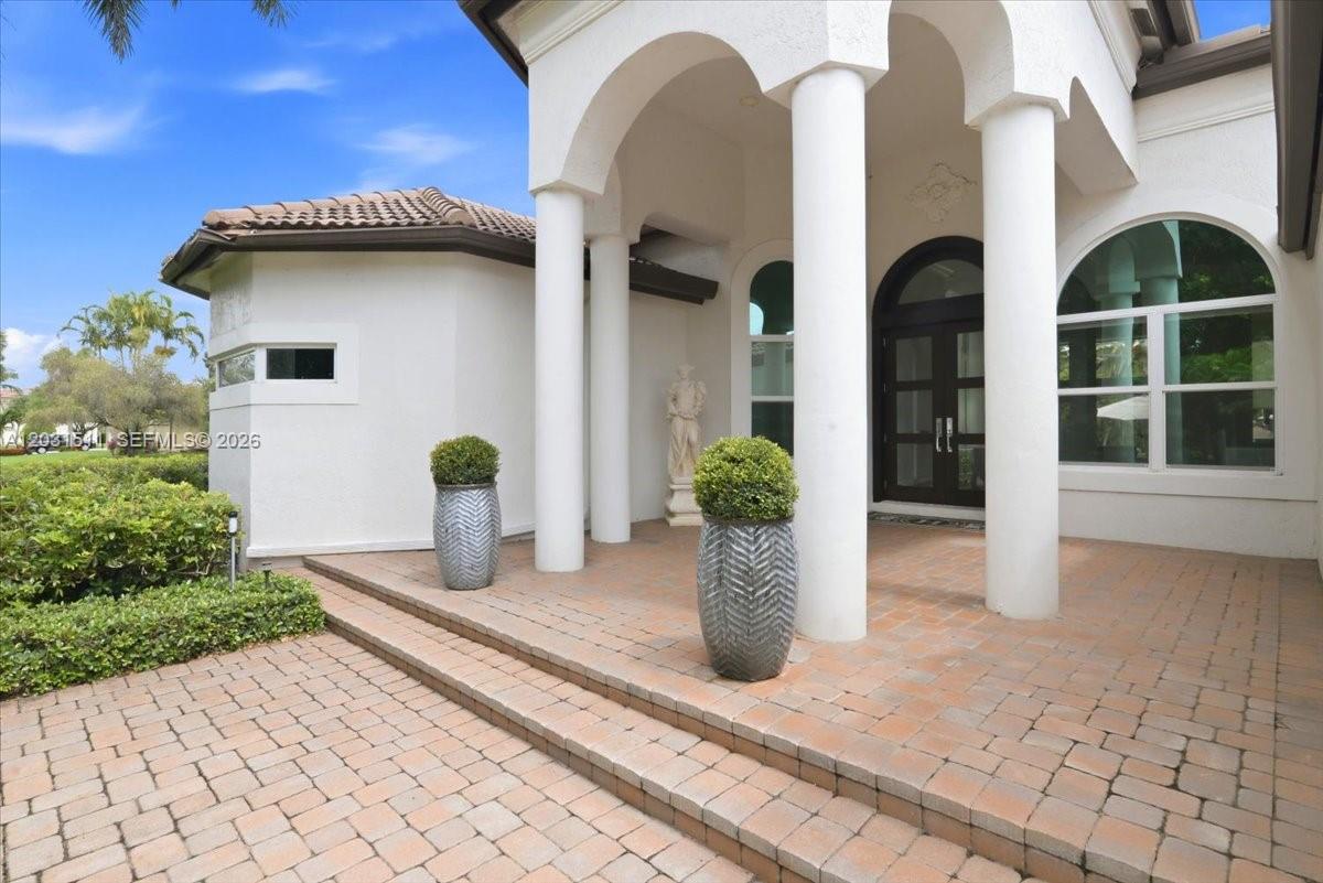 A paved walkway leads to a covered entryway with white columns and two potted plants — 12160 NW 18th St, Plantation FL 33323, PLANTATION, FL