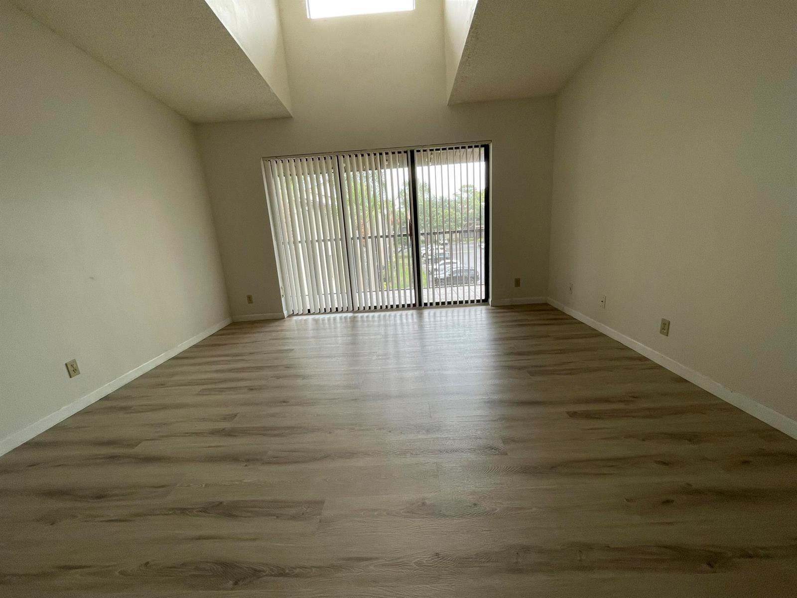 An empty room features light wood-look flooring, white walls, a vaulted ceiling, and sliding glass doors — 207 Foxtail Drive # E3, FL 33415, FL
