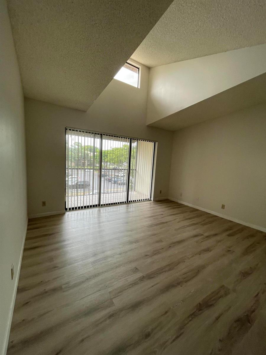An empty room features light wood-look flooring, a vaulted ceiling, and a large sliding glass door — 207 Foxtail Drive # E3, FL 33415, FL