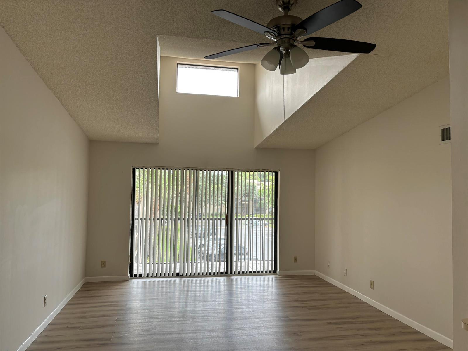 An empty living room with vaulted ceilings, a ceiling fan, sliding glass doors, and wood-look flooring — 207 Foxtail Drive # E3, FL 33415, FL
