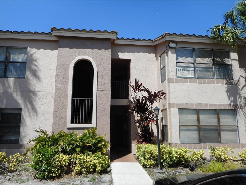 The exterior of a two-story apartment building features beige stucco walls and a tiled roof — 2736 S University Drive # 1104, Davie FL 33328, DAVIE, FL