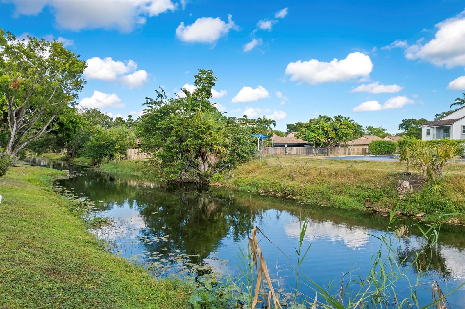 A narrow canal flows through a grassy residential area under a bright, cloudy sky — 2736 S University Drive # 1104, Davie FL 33328, DAVIE, FL
