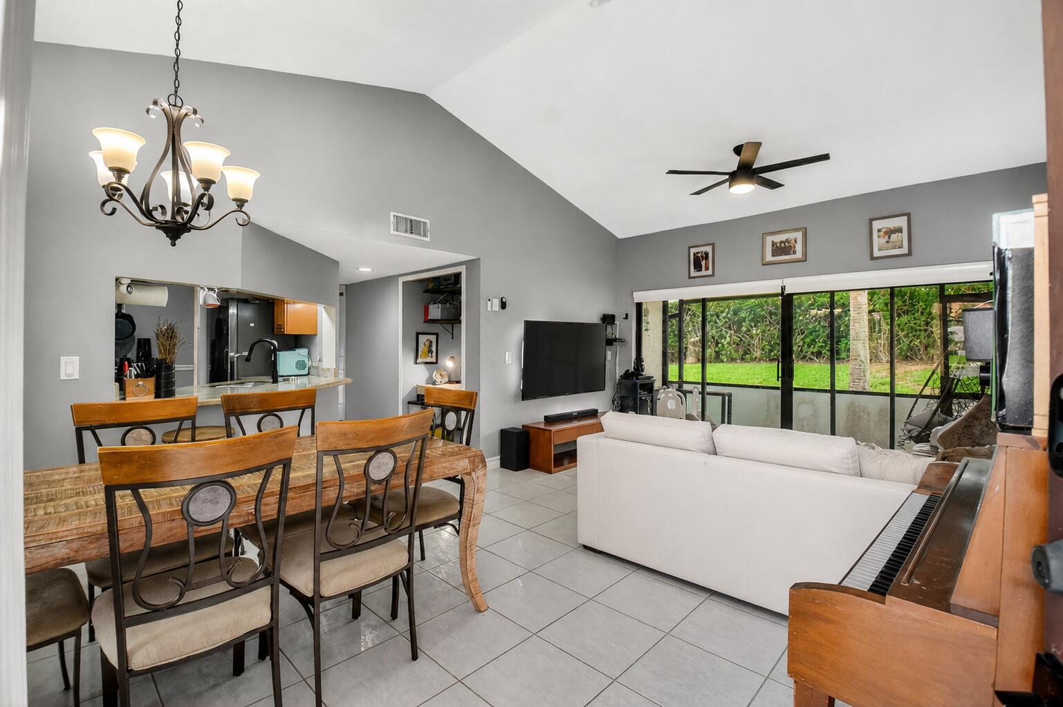 A living and dining area with vaulted ceilings, tile floors, and a sliding glass door — 14 Via De Casas Sur # 104, Boynton Beach FL 33426, BOYNTON BEACH, FL