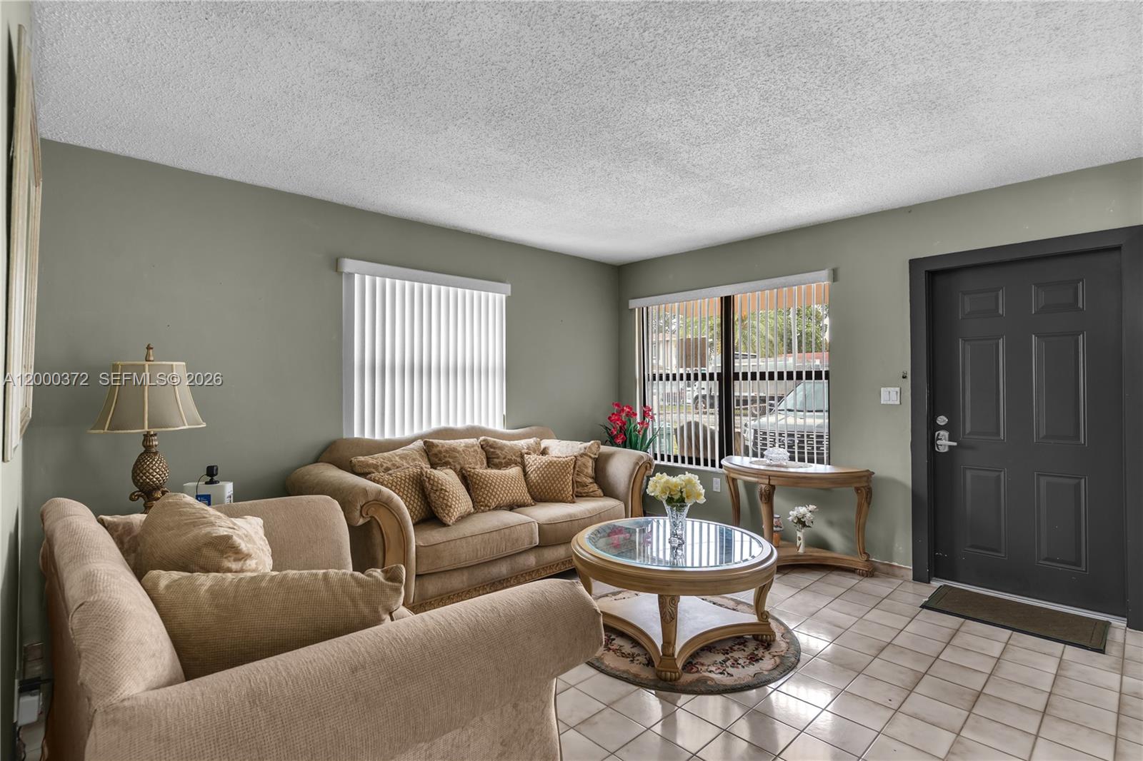 A living room features beige furniture, a glass-topped coffee table, tile flooring, and a dark door — 6770 SW 15th St, Miami FL 33144, MIAMI, FL