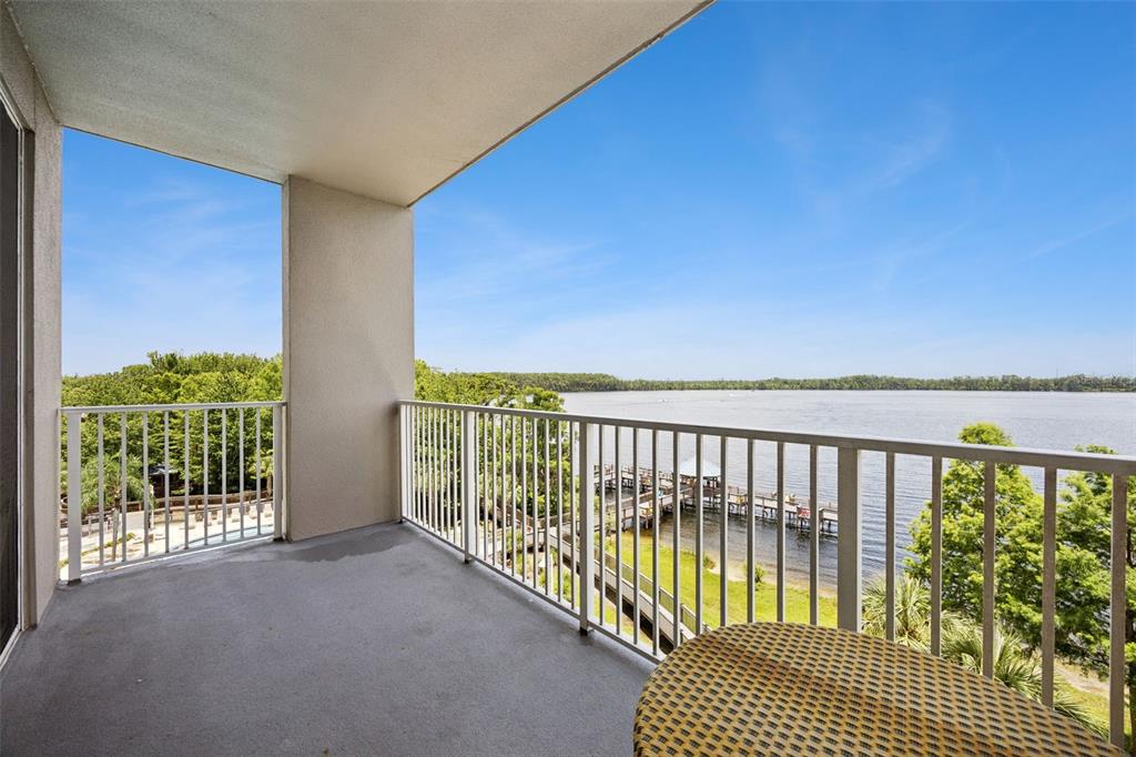 A covered balcony overlooks a lake with a wooden dock and surrounding trees — 13427 BLUE HERON BEACH DRIVE UNIT 301, ORLANDO, FL