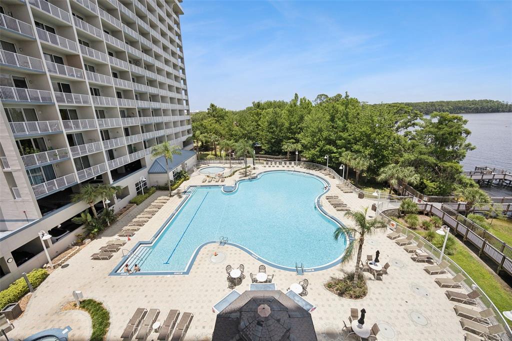An elevated view shows a large swimming pool next to a multi-story building and water — 13427 BLUE HERON BEACH DRIVE UNIT 301, ORLANDO, FL