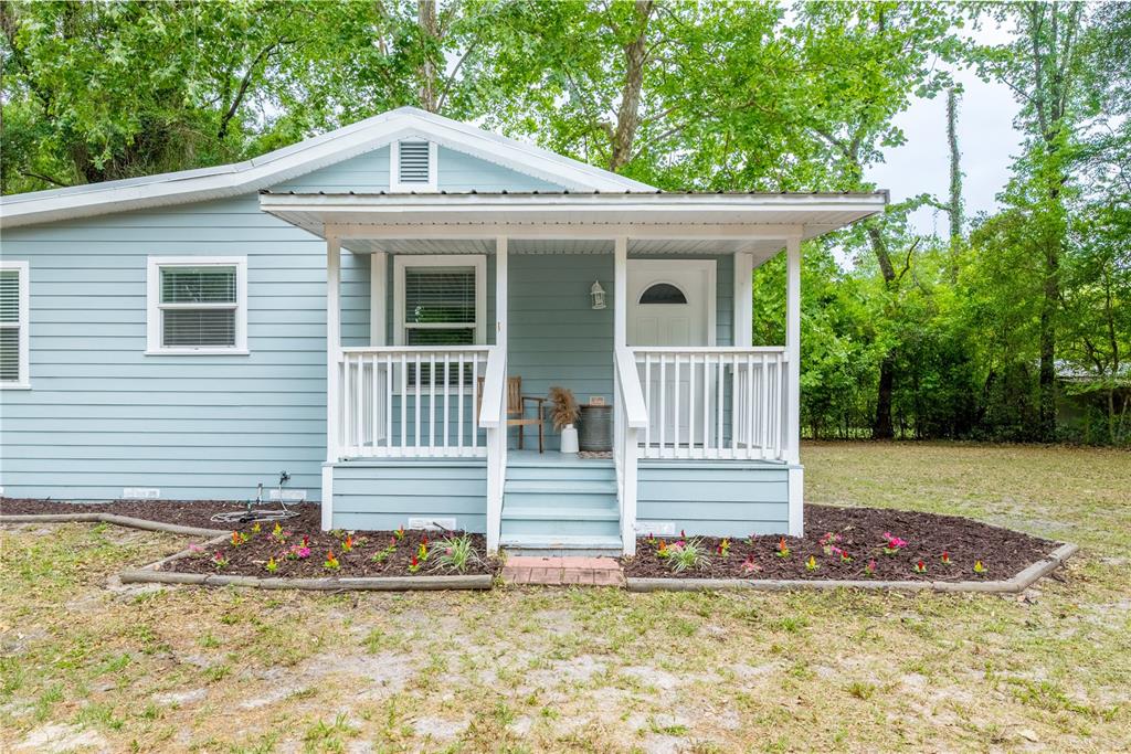A light blue house features a front porch with white railings and a small garden — 16619 NW STATE ROAD 45, HIGH SPRINGS, FL