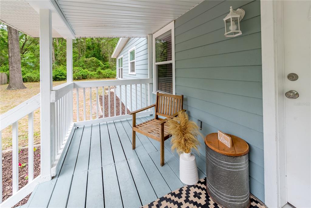 A light blue covered porch features a wooden chair, a decorative vase, and a metal stool — 16619 NW STATE ROAD 45, HIGH SPRINGS, FL