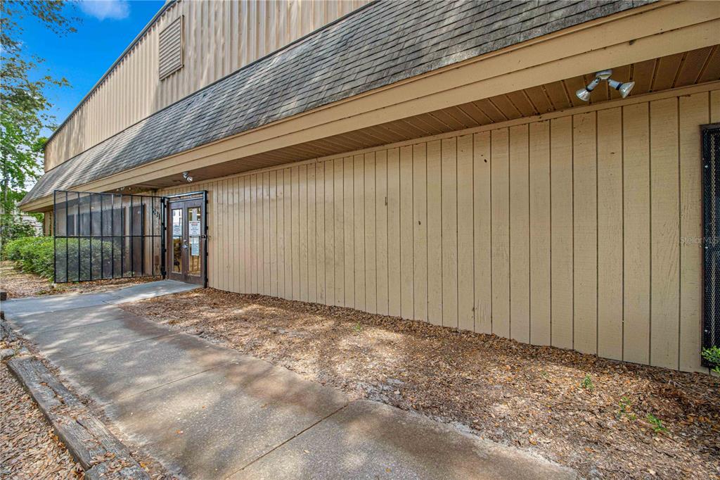 A beige vertical-sided building exterior features a shingled roof, a concrete walkway, and double doors — 1031 NE 16TH STREET, OCALA, FL