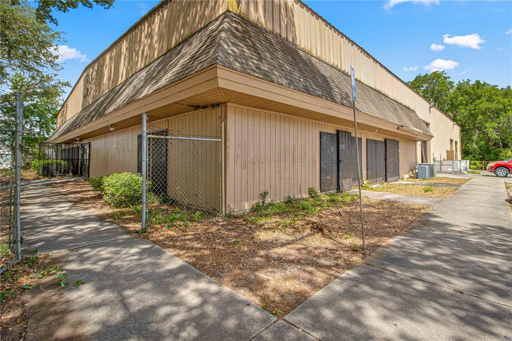 A low-angle exterior view of a tan commercial building with a chain-link fence and sidewalk — 1031 NE 16TH STREET, OCALA, FL