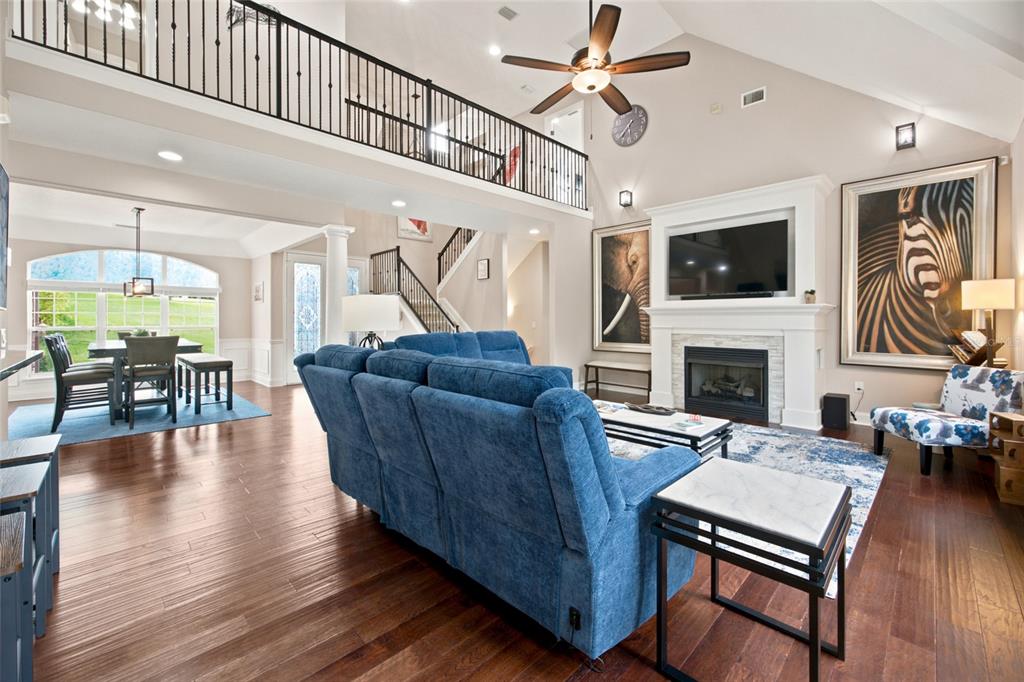 A spacious living room with a blue sofa, fireplace, and a lofted balcony above — 1706 SW 27TH STREET, OCALA, FL