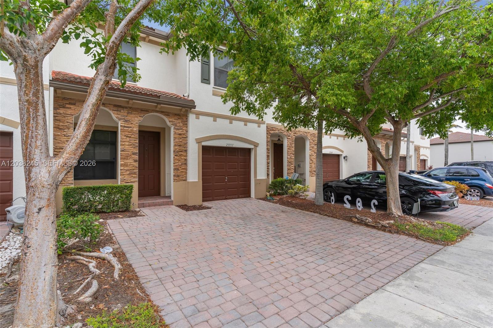 A two-story townhouse features a brick driveway, a brown garage door, and stone accents — 23357 SW 113th Psge, Homestead FL 33032, HOMESTEAD, FL