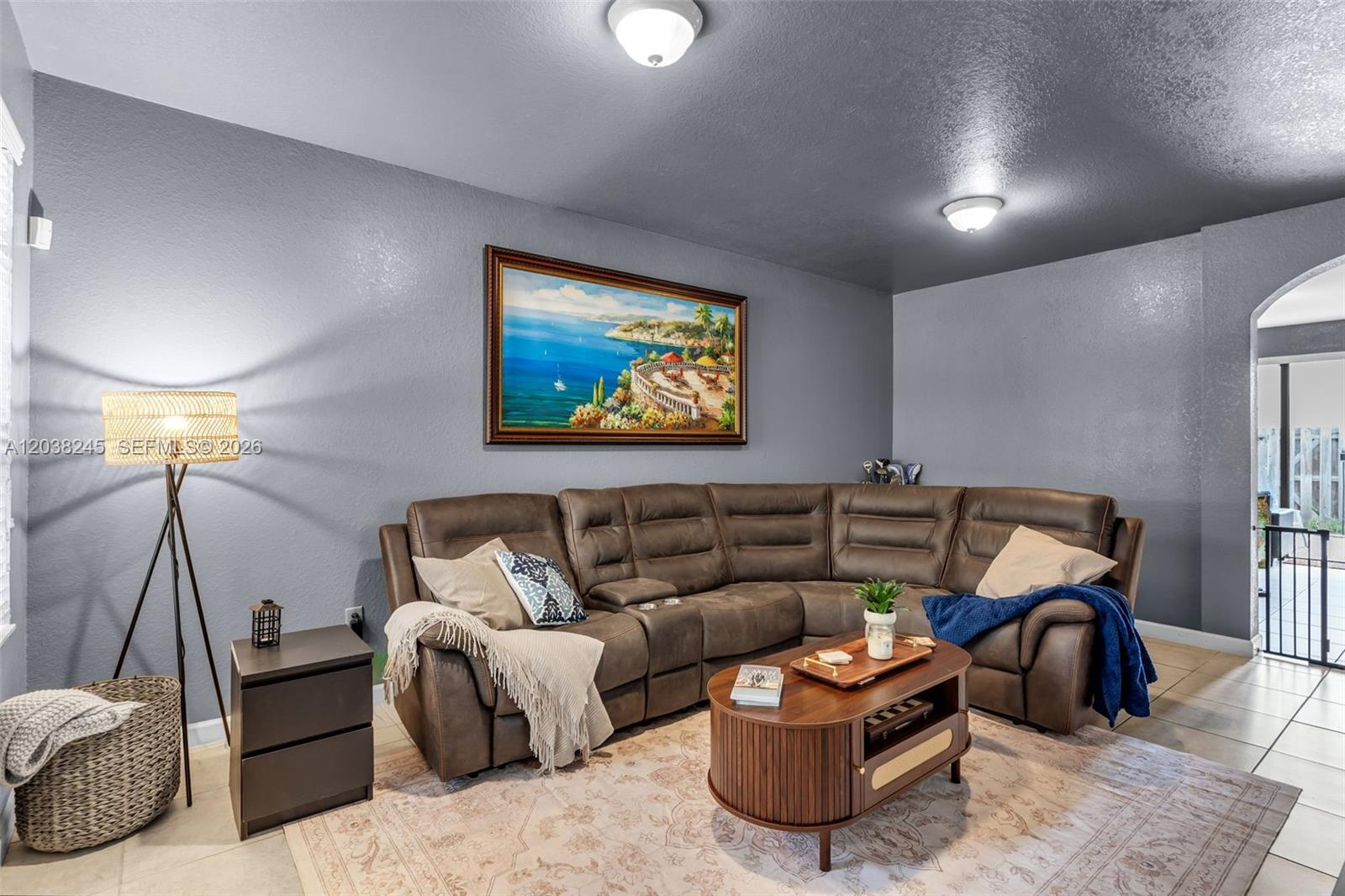 A living room features a brown sectional sofa, a coffee table, and a coastal landscape painting — 23357 SW 113th Psge, Homestead FL 33032, HOMESTEAD, FL