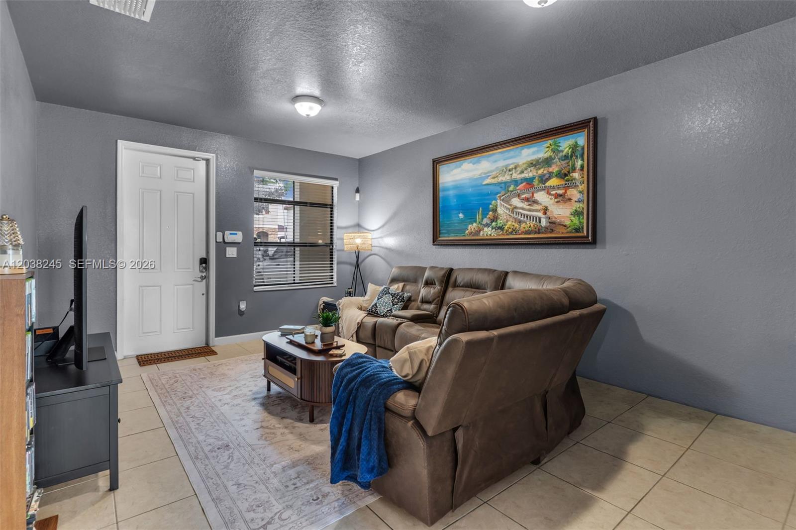A living room features a brown sectional sofa, a coffee table, and a large coastal painting — 23357 SW 113th Psge, Homestead FL 33032, HOMESTEAD, FL