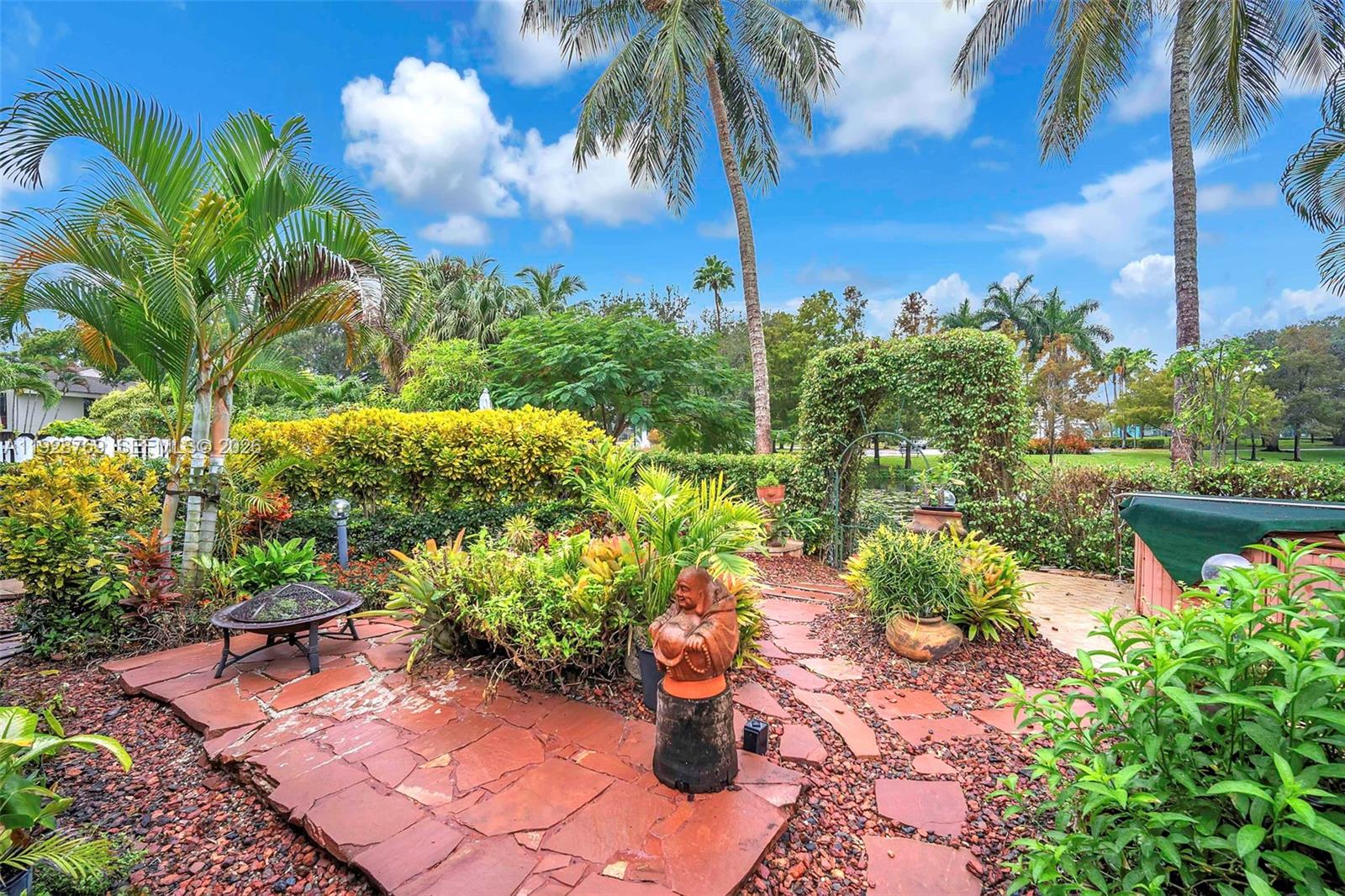 A landscaped backyard features a stone patio, a Buddha statue, and lush tropical foliage — 113 NW 73rd Ter, Plantation FL 33317, PLANTATION, FL