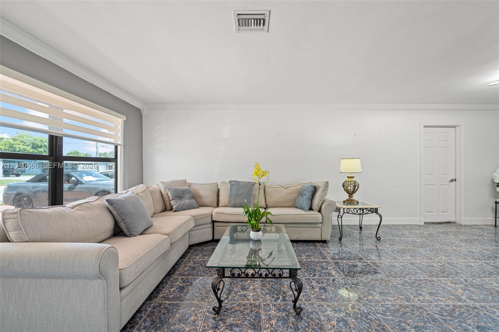A living room features a beige sectional sofa, glass coffee table, and dark tiled floors — 7701 W 16th Ct, Hialeah FL 33014, HIALEAH, FL