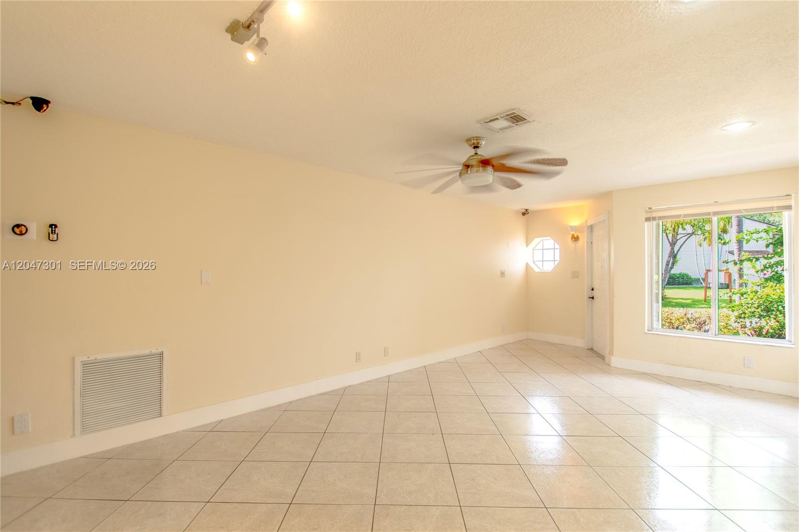 A bright, empty room features light-colored tile flooring, a ceiling fan, and a large window — 9803 NW 37th St, Sunrise FL 33351, SUNRISE, FL