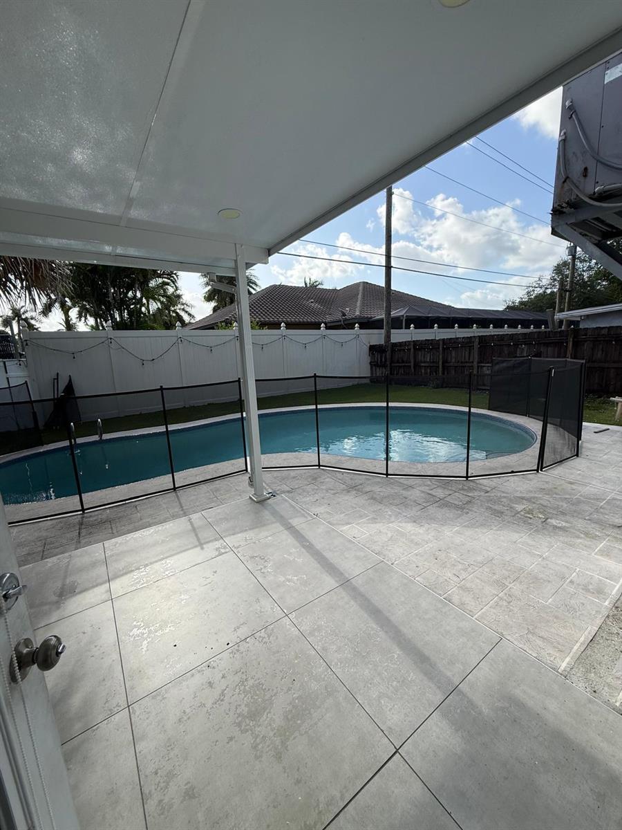 A backyard features a swimming pool enclosed by a black mesh safety fence and patio — 3111 N 66th Avenue, Hollywood FL 33024, HOLLYWOOD, FL