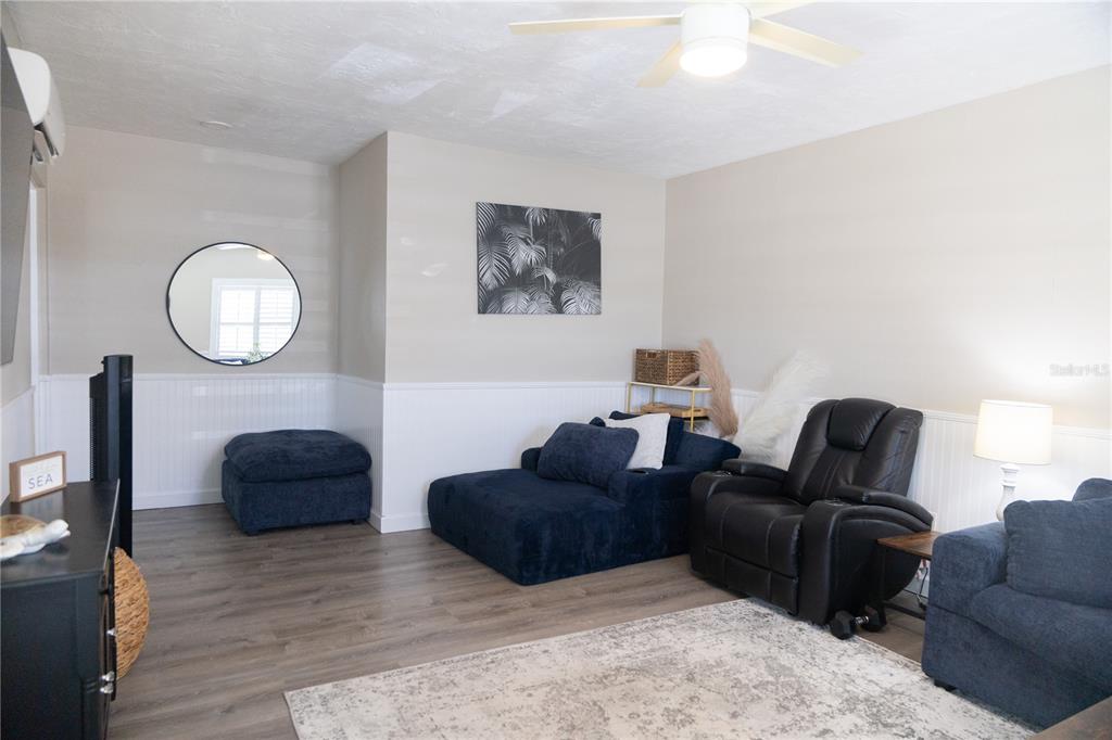 A living room features wood-look flooring, white wainscoting, a ceiling fan, and dark blue seating — 136 MARYLAND AVENUE, PALM HARBOR, FL