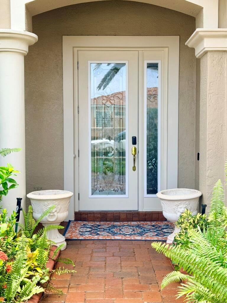 A front entryway features a beige door with glass panels, brick flooring, and two planters — 9546 LANTERN BAY Circle, West Palm Beach FL 33411, WEST PALM BEACH, FL