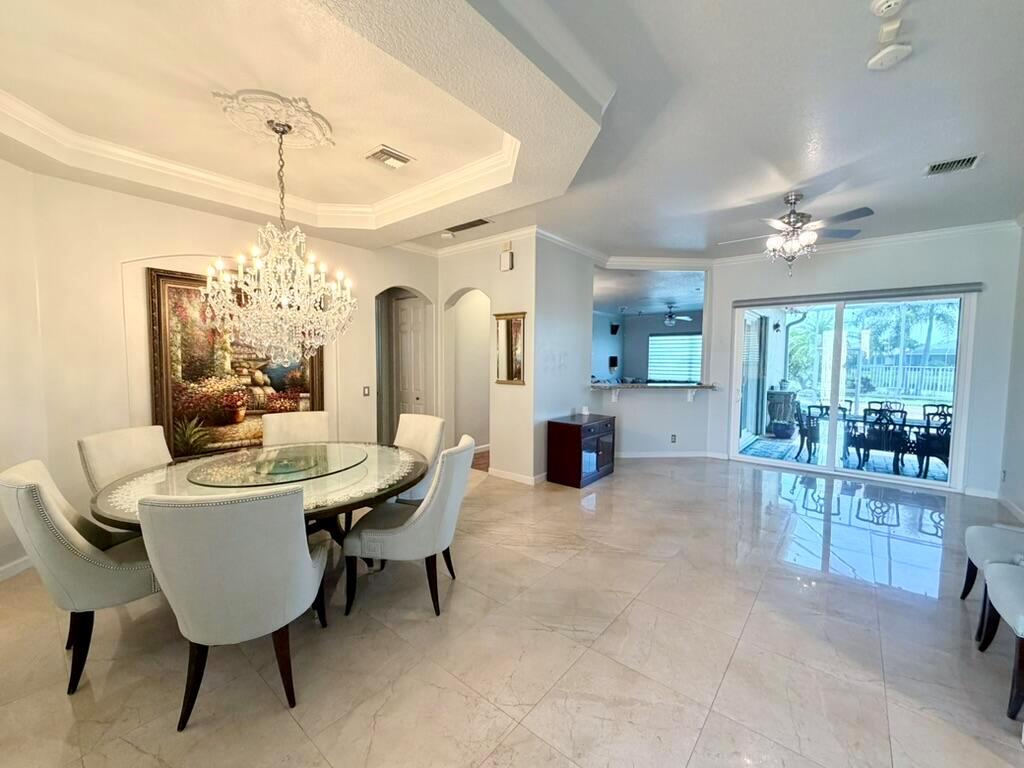 A dining room with a crystal chandelier, glass table, and tile flooring leads to a patio — 9546 LANTERN BAY Circle, West Palm Beach FL 33411, WEST PALM BEACH, FL