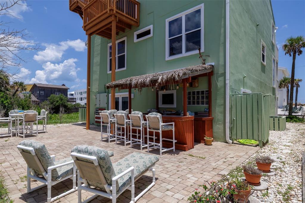 A green house exterior features a paved patio with a tiki bar and lounge seating — 6854 S ATLANTIC AVENUE, NEW SMYRNA BEACH, FL