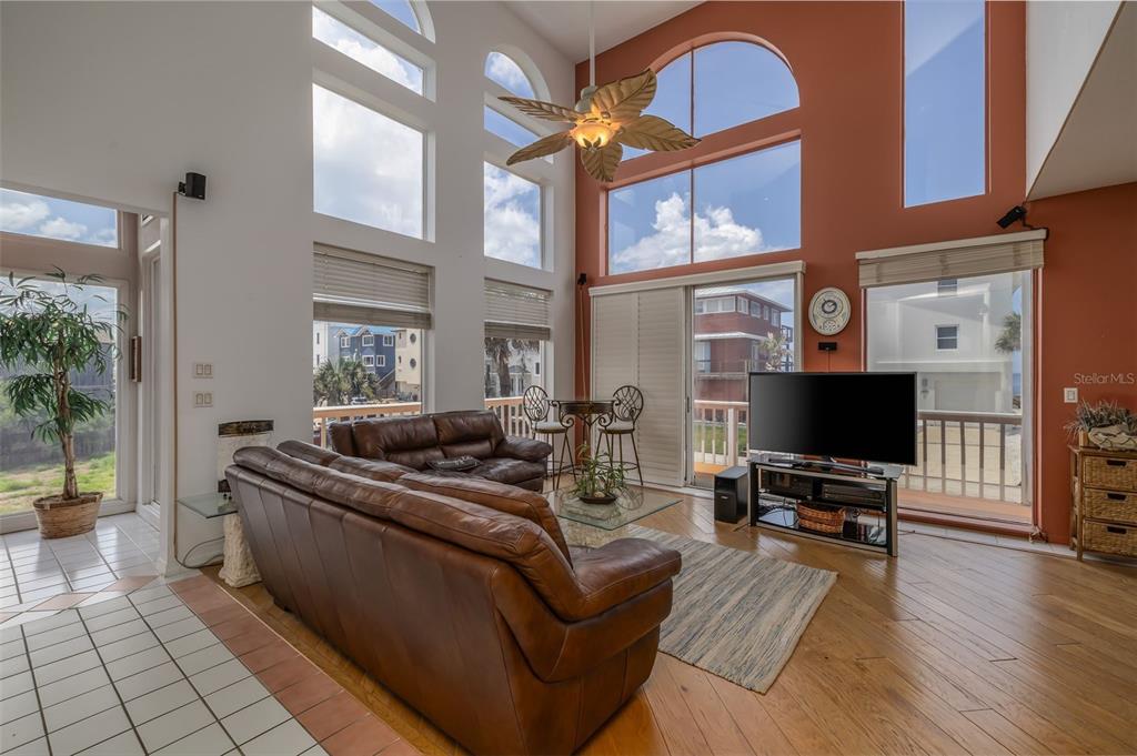 A living room features tall arched windows, a brown leather sofa, and hardwood flooring — 6854 S ATLANTIC AVENUE, NEW SMYRNA BEACH, FL