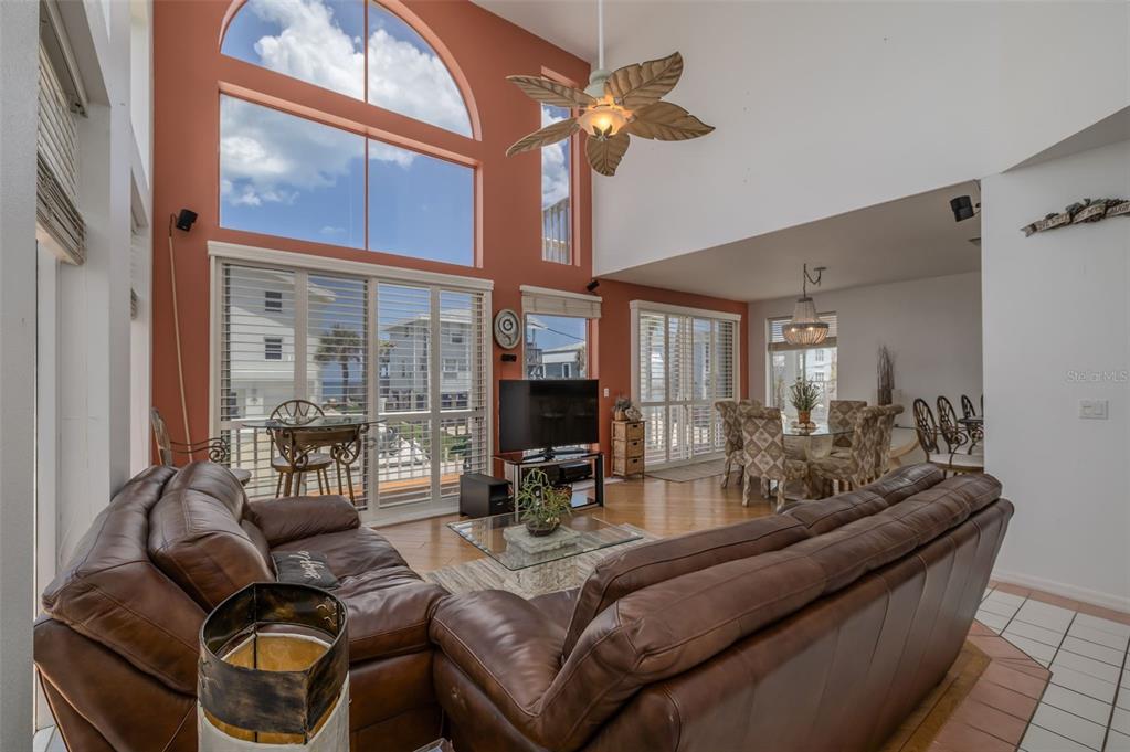 A living room with high ceilings, large windows, a ceiling fan, and brown leather sofas — 6854 S ATLANTIC AVENUE, NEW SMYRNA BEACH, FL