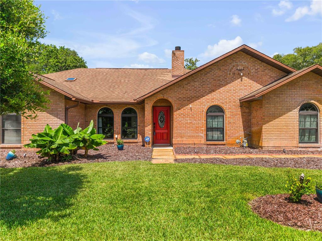 A single-story brick house features a red front door and a brown shingled roof — 171 LIVE OAK COURT, NEW SMYRNA BEACH, FL
