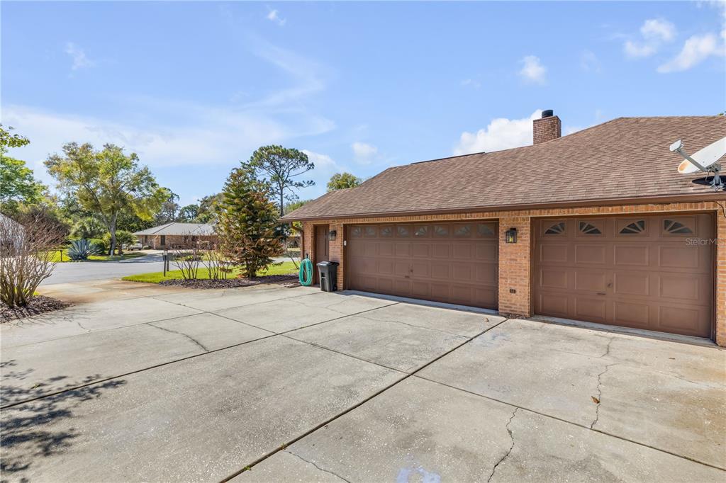 A brick house exterior features a two-car garage, a concrete driveway, and a shingled roof — 171 LIVE OAK COURT, NEW SMYRNA BEACH, FL
