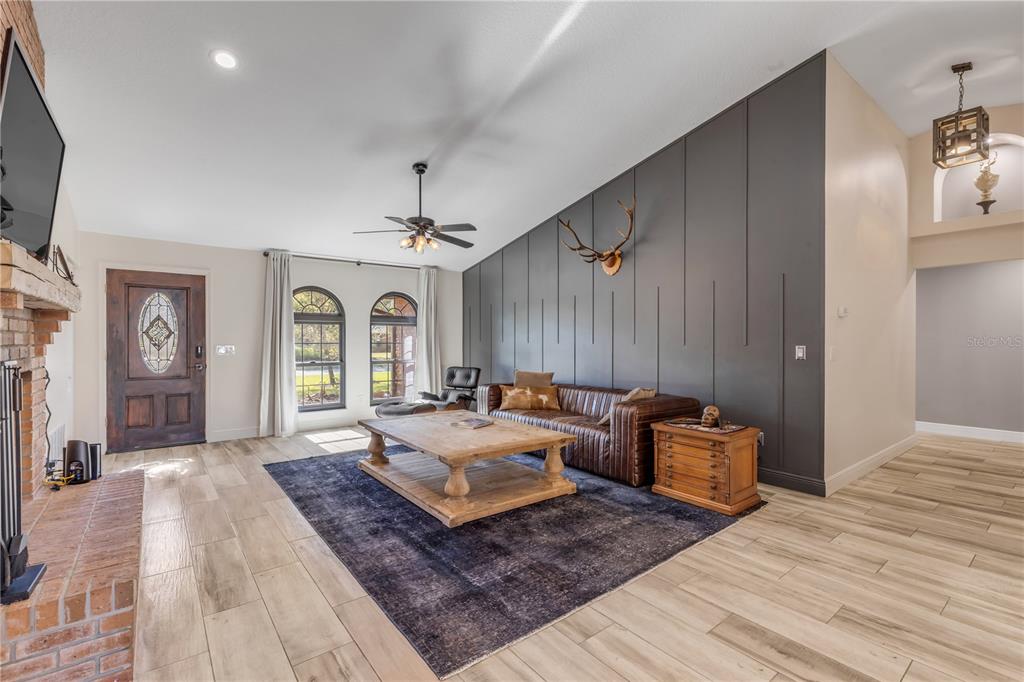 A living room features a dark gray accent wall, a leather sofa, and wood-look flooring — 171 LIVE OAK COURT, NEW SMYRNA BEACH, FL