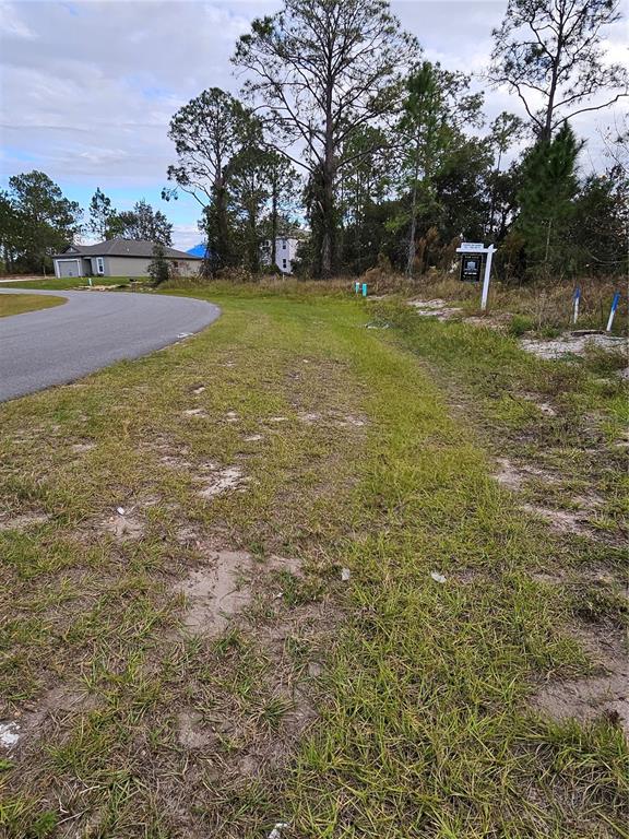 A vacant, grassy residential lot features a real estate sign and surrounding trees — 361 BASS COURT, POINCIANA, FL