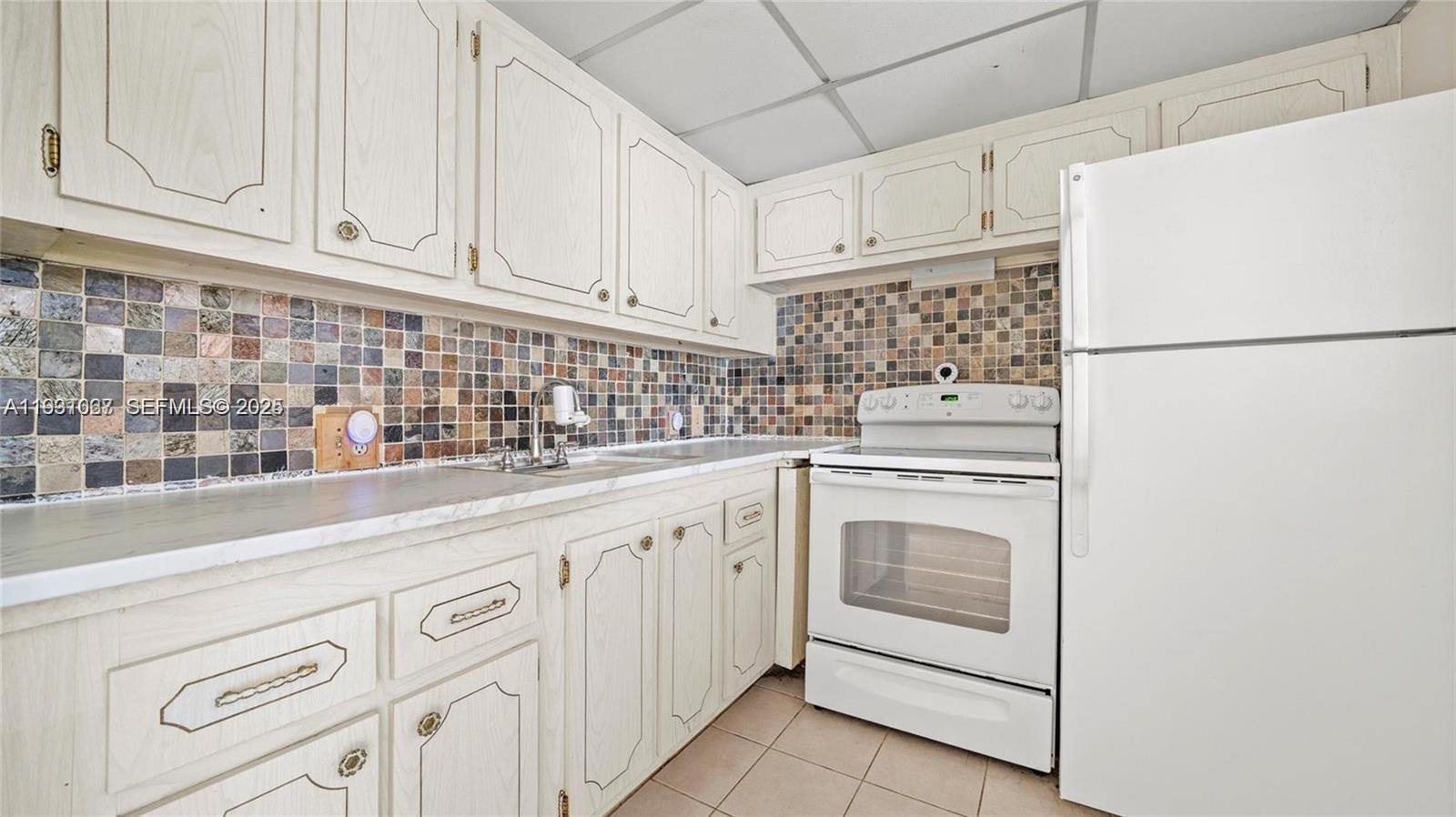 A kitchen features white cabinets, a multi-colored mosaic tile backsplash, and white appliances — 79 Suffolk B # 79, Boca Raton FL 33434, BOCA RATON, FL