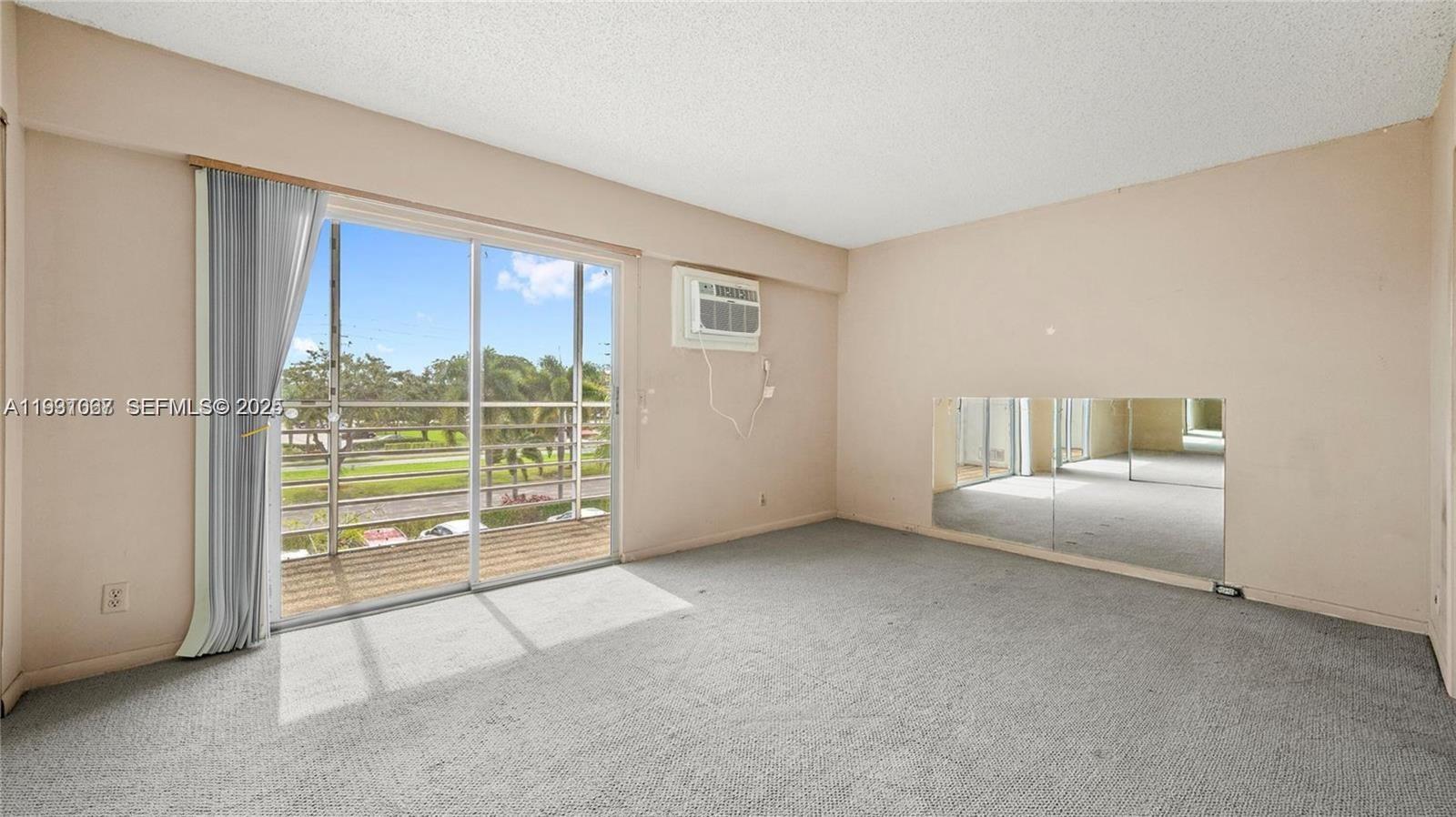 An empty room features gray carpeting, a sliding glass door to a balcony, and mirrors — 79 Suffolk B # 79, Boca Raton FL 33434, BOCA RATON, FL