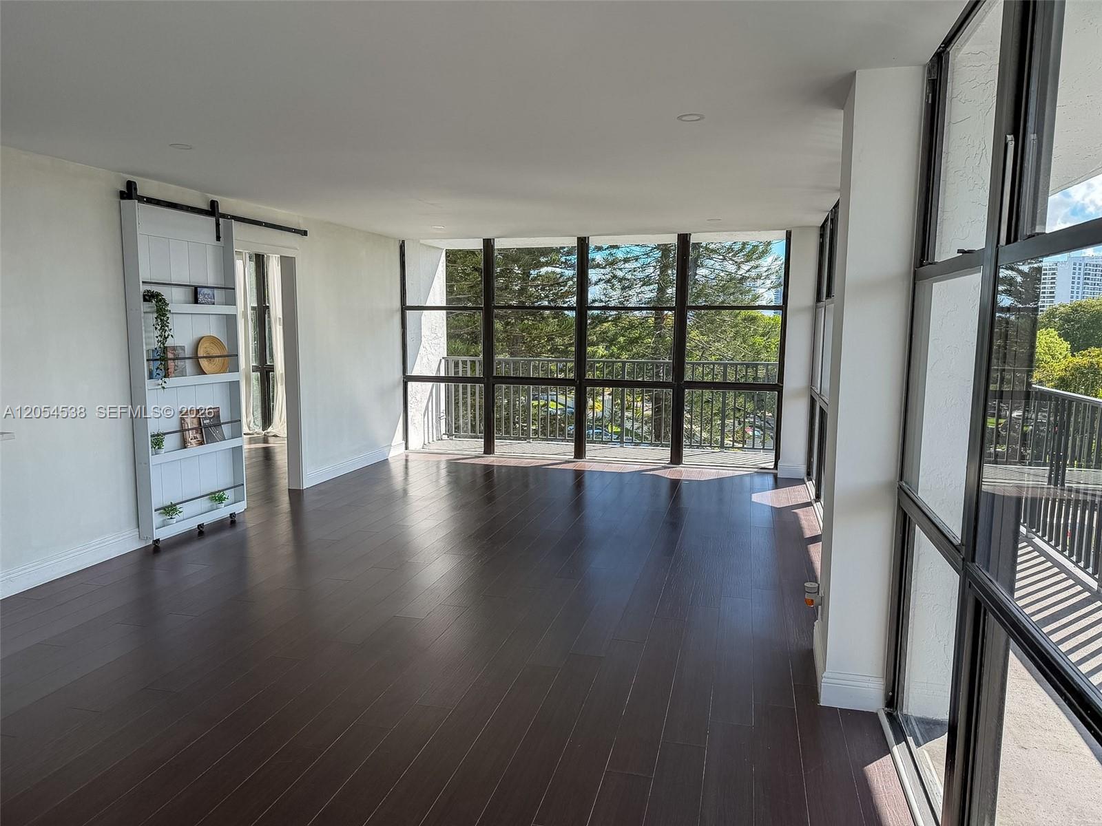 A bright, empty room features dark wood flooring, floor-to-ceiling windows, and a white sliding bookshelf — 1000 Parkview Dr # 531, Hallandale Beach FL 33009, HALLANDALE BEACH, FL