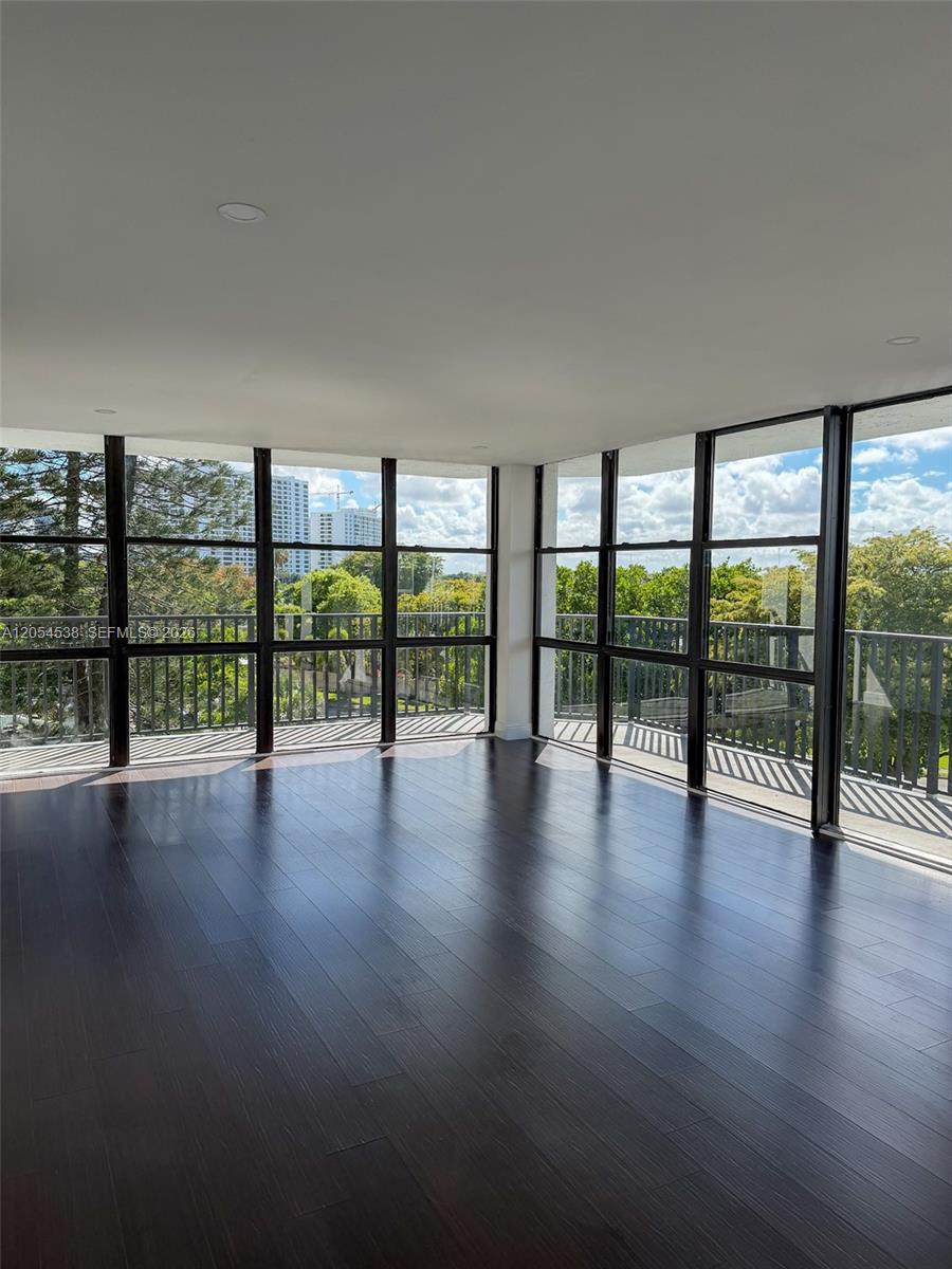 An empty room with dark wood flooring and floor-to-ceiling windows overlooking trees and buildings — 1000 Parkview Dr # 531, Hallandale Beach FL 33009, HALLANDALE BEACH, FL