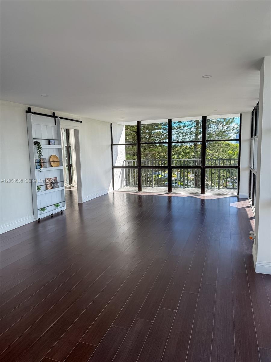 An empty room features dark wood flooring, white walls, a sliding bookshelf, and floor-to-ceiling windows — 1000 Parkview Dr # 531, Hallandale Beach FL 33009, HALLANDALE BEACH, FL