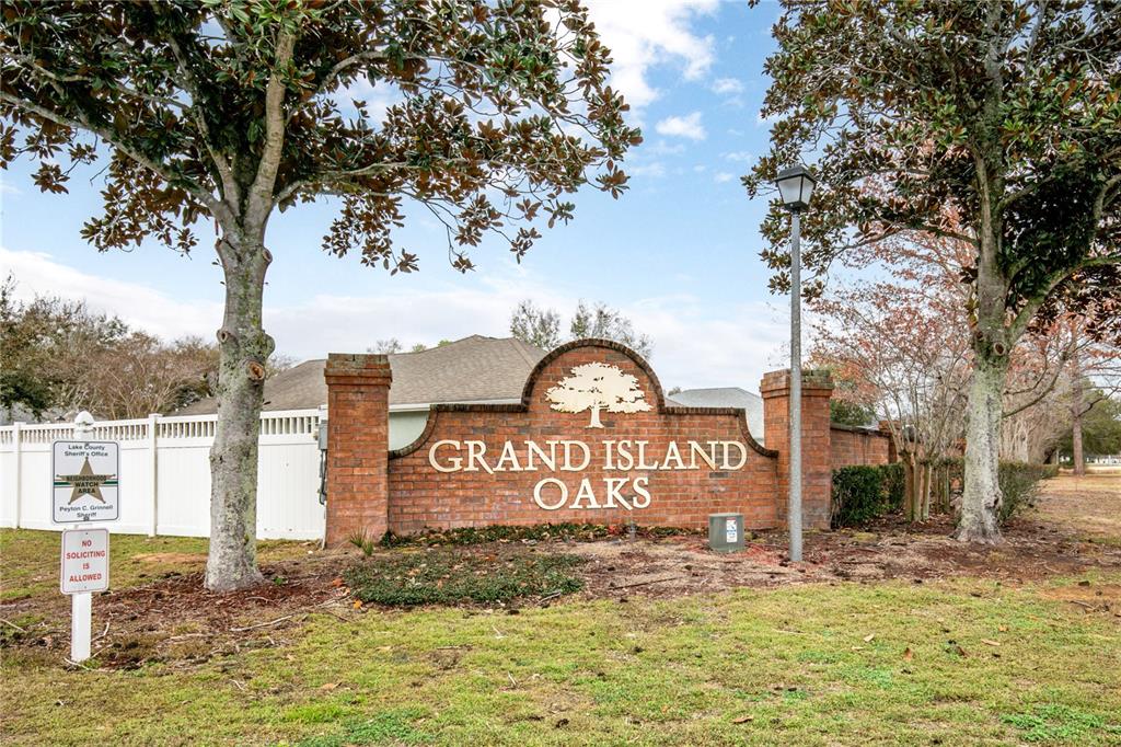 A brick monument sign for Grand Island Oaks stands in front of a white fence — 36452 GRAND ISLAND OAKS CIRCLE, GRAND ISLAND, FL