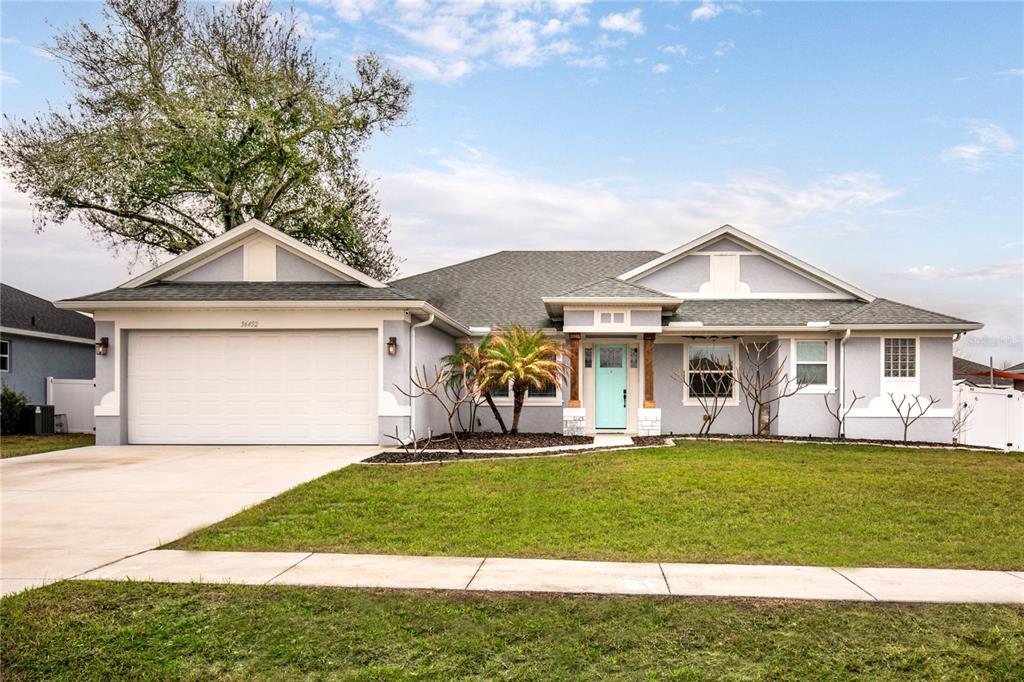 A single-story house with a light blue front door, a two-car garage, and a lawn — 36452 GRAND ISLAND OAKS CIRCLE, GRAND ISLAND, FL