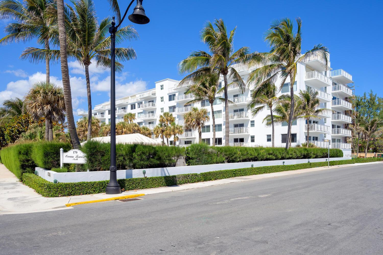 A multi-story white apartment building with balconies stands behind a hedge and palm trees — 170 N Ocean Boulevard # 511, Palm Beach FL 33480, PALM BEACH, FL