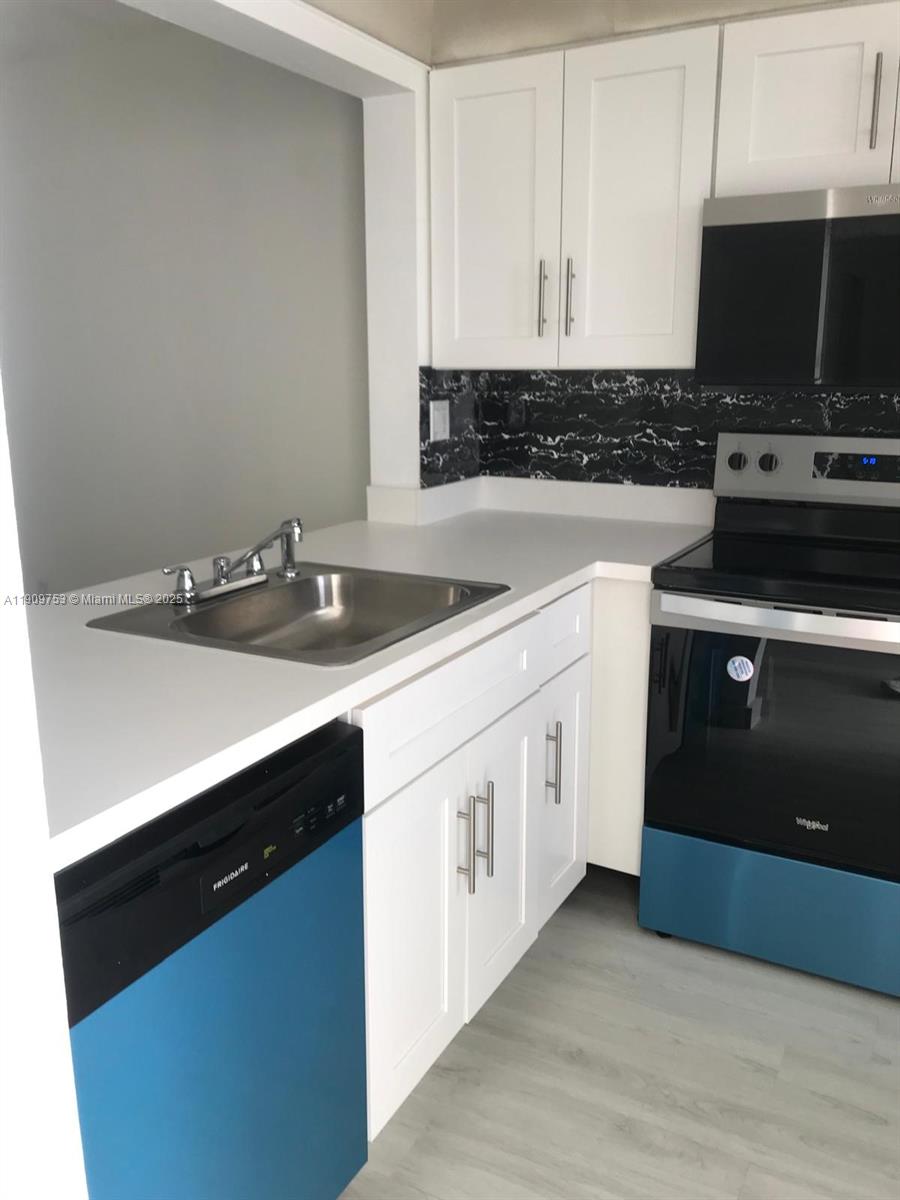 A kitchen features white cabinets, a stainless steel sink, and black appliances with blue protective film — 438 NE 210th Cir Ter # 4B, Miami FL 33179, MIAMI, FL