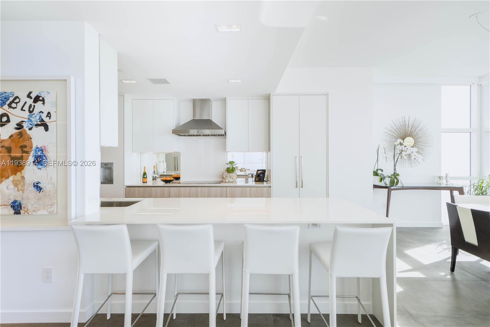 A modern kitchen features white cabinetry, a large island with bar stools, and stainless appliances — 6103 Aqua Ave # 701, Miami Beach FL 33141, MIAMI BEACH, FL