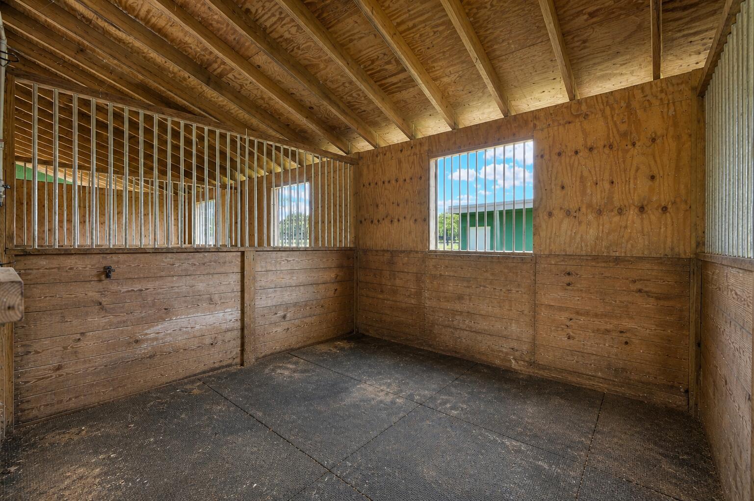 An empty horse stall features wood-paneled walls, metal bars, and black rubber floor mats — 16031 Rustic Road, Wellington FL 33470, WELLINGTON, FL