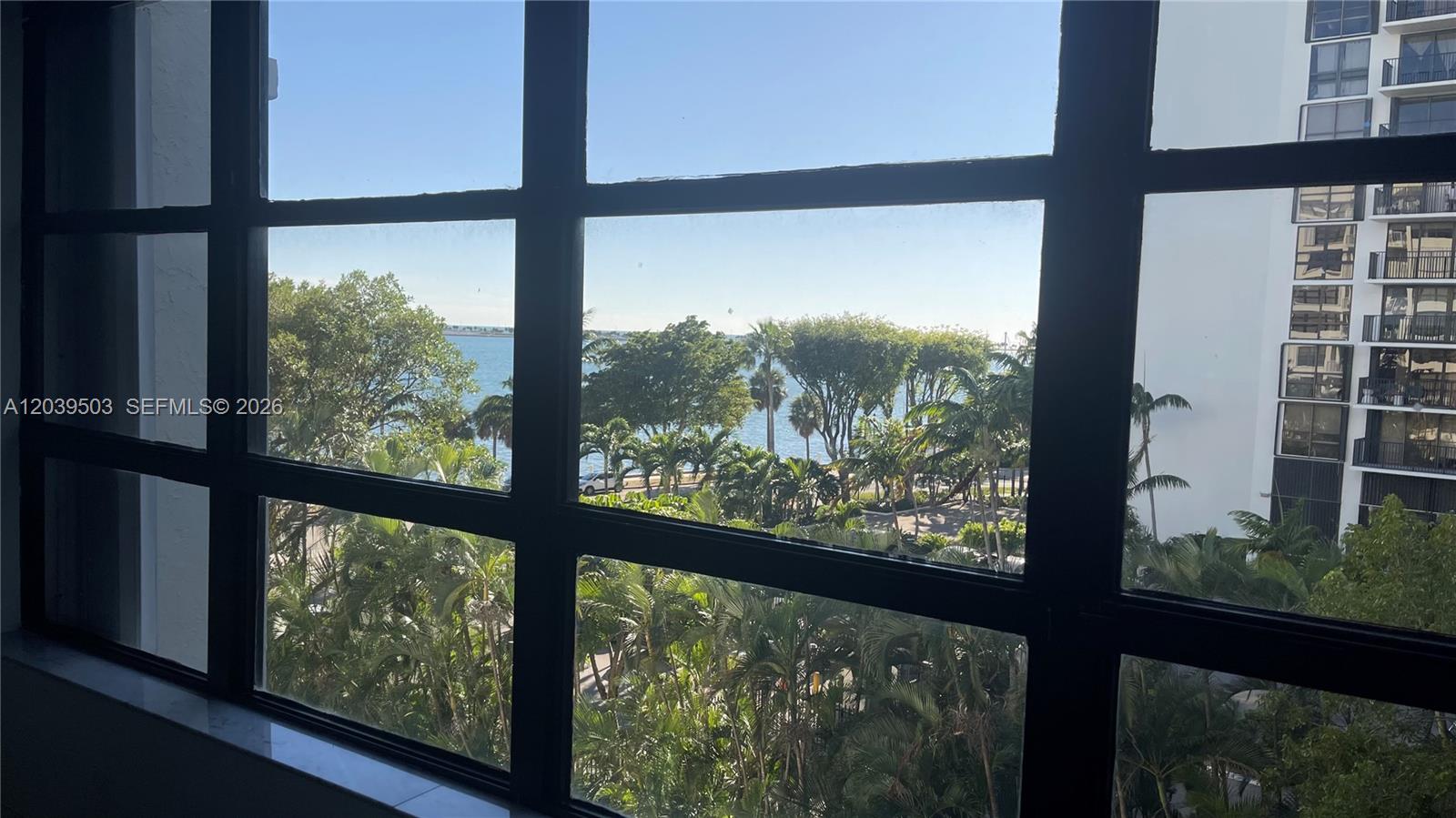 A view of the ocean and palm trees is visible through a large grid window — 1440 Brickell Bay Dr # 508, Miami FL 33131, MIAMI, FL