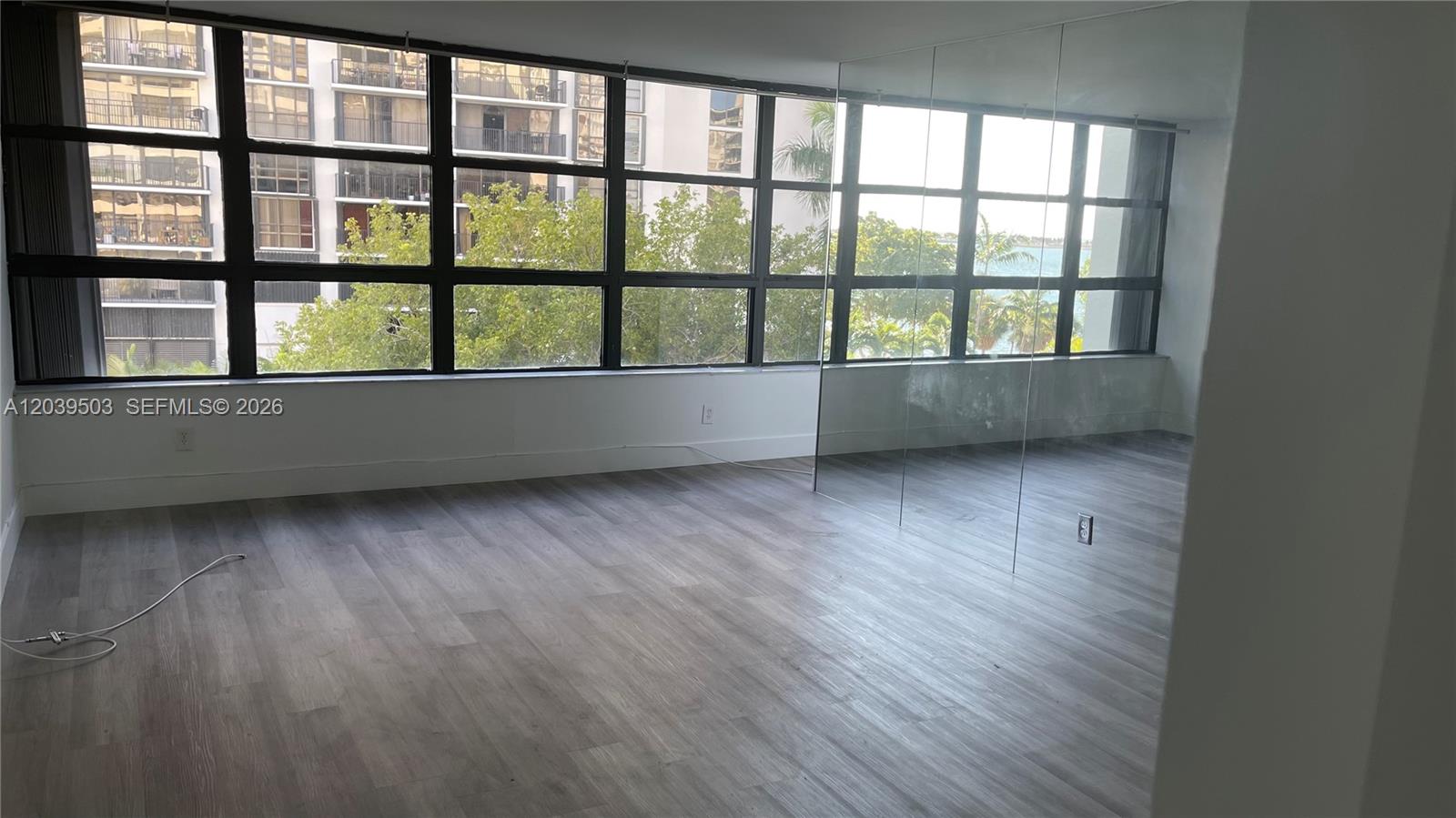 An empty room features wood-look flooring, a large window wall, and a mirrored wall section — 1440 Brickell Bay Dr # 508, Miami FL 33131, MIAMI, FL