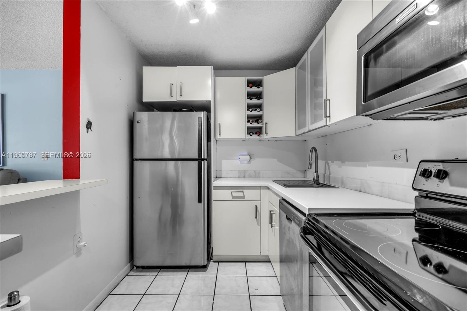 A compact kitchen features white cabinets, stainless steel appliances, and white tiled flooring — 7060 NW 179th St # 210, Hialeah FL 33015, HIALEAH, FL