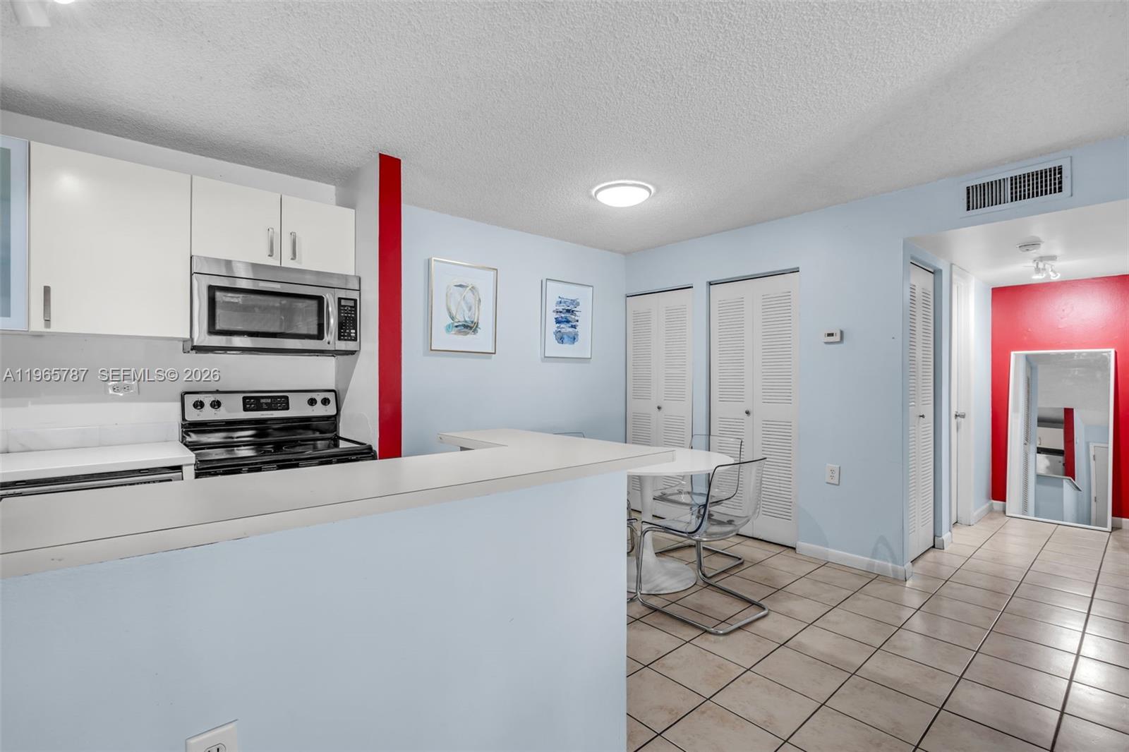 A kitchen with white cabinets and a breakfast bar overlooks a dining area with tile floors — 7060 NW 179th St # 210, Hialeah FL 33015, HIALEAH, FL